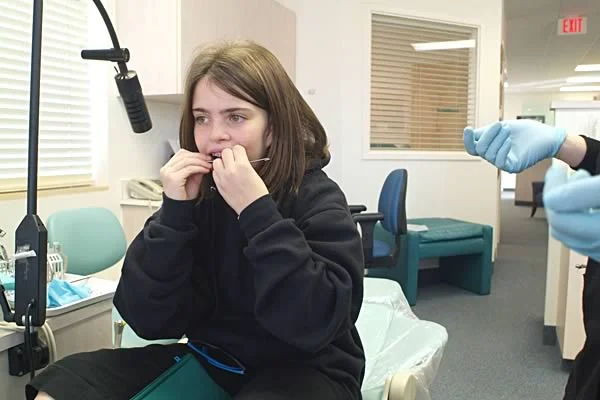 A girl putting her headgear facebow in place: For patients age ~7-11, directions still need to be concrete. This girl is more likely to wear her headgear if instructions are given to her in this way.